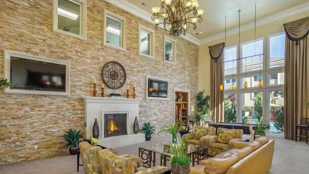 A spacious living room with a stone wall, fireplace, comfortable seating, and large windows.