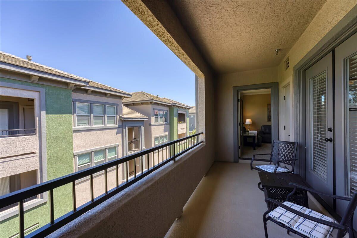 A balcony with a view of neighboring buildings, a door, and two chairs.