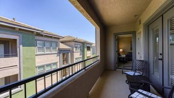 A balcony with a view of neighboring buildings, a door, and two chairs.