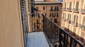 Un balcón estrecho con baranda de metal que da a una calle con edificios.