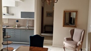 Cocina moderna con armarios grises, horno empotrado y pileta de acero inoxidable. Hay un comedor con mesa de madera y una silla azul. Un candelabro cuelga sobre la mesa del comedor.