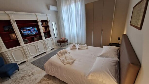 Habitación de hotel con una cama grande, un televisor montado en un mueble, un armario y un escritorio con lámpara.