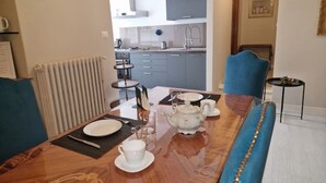 Un comedor con una mesa de madera dispuesta para dos personas, una silla tapizada de azul y vistas a una cocina con electrodomésticos modernos.