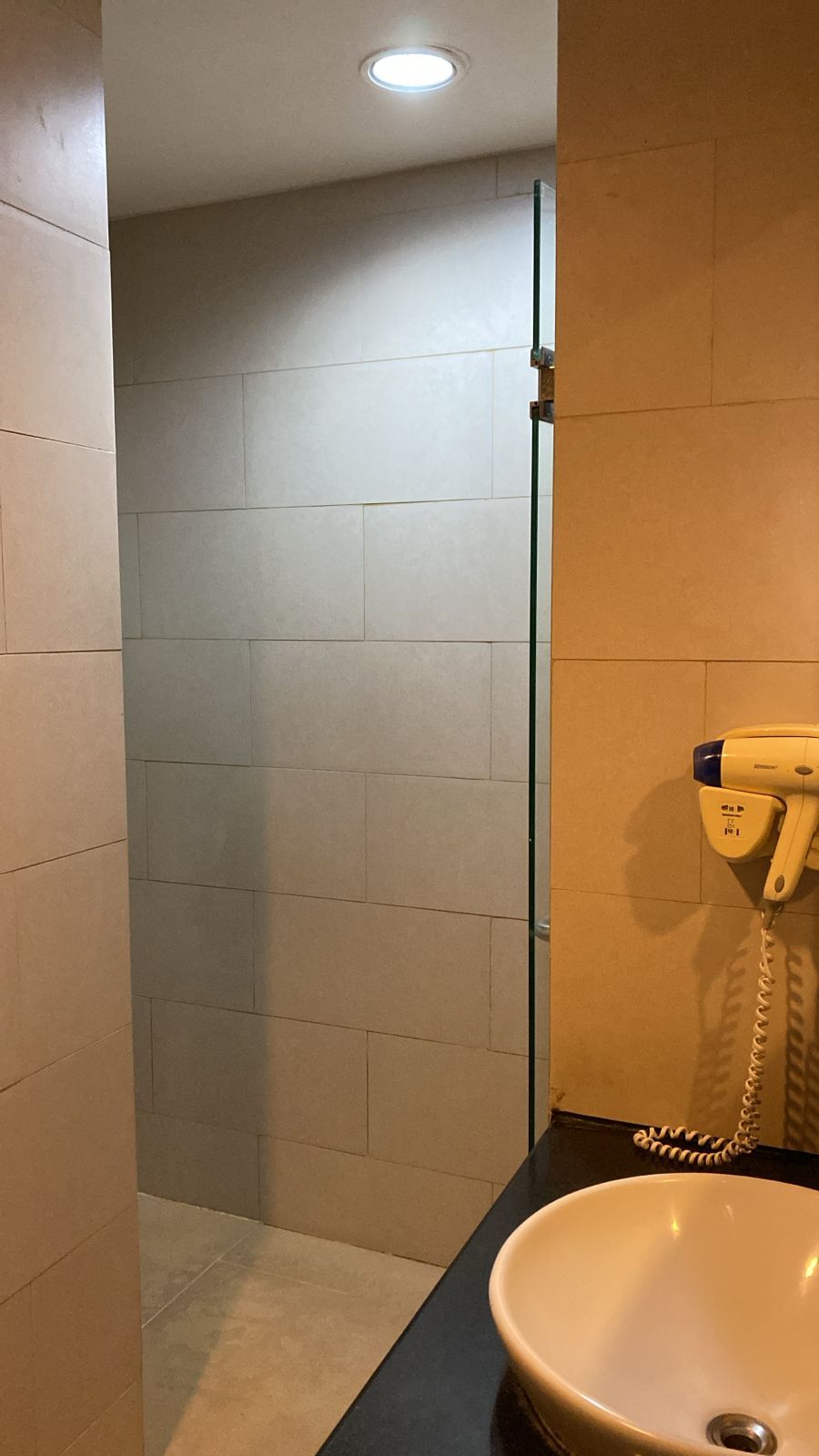 A bathroom with a glass shower door, a sink, and a telephone mounted on the wall.