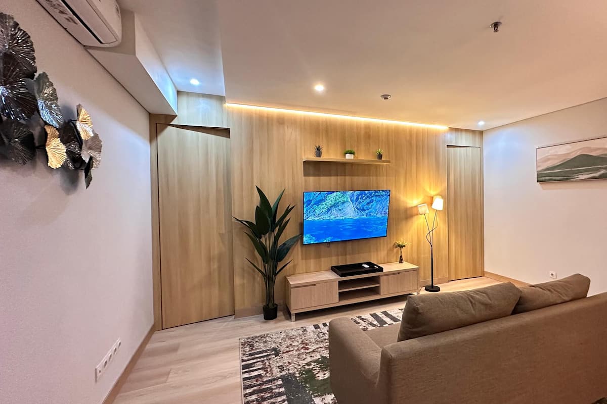 A modern living room with a flat-screen TV, a sofa, a plant, and a painting on the wall.