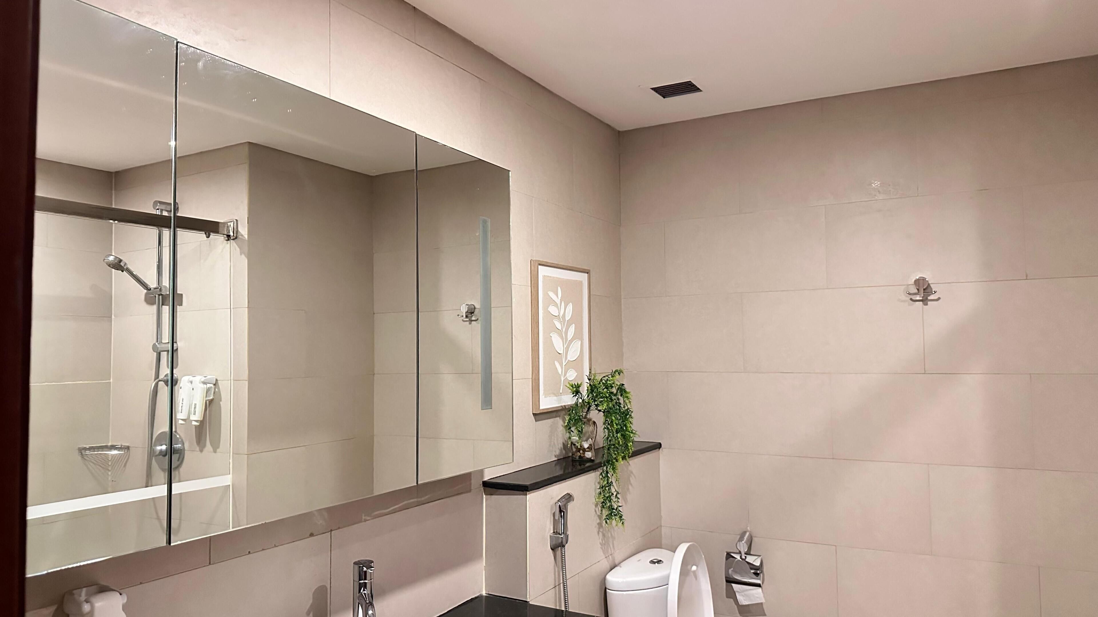 A modern bathroom with a large mirror, a shower, a toilet, and a sink.