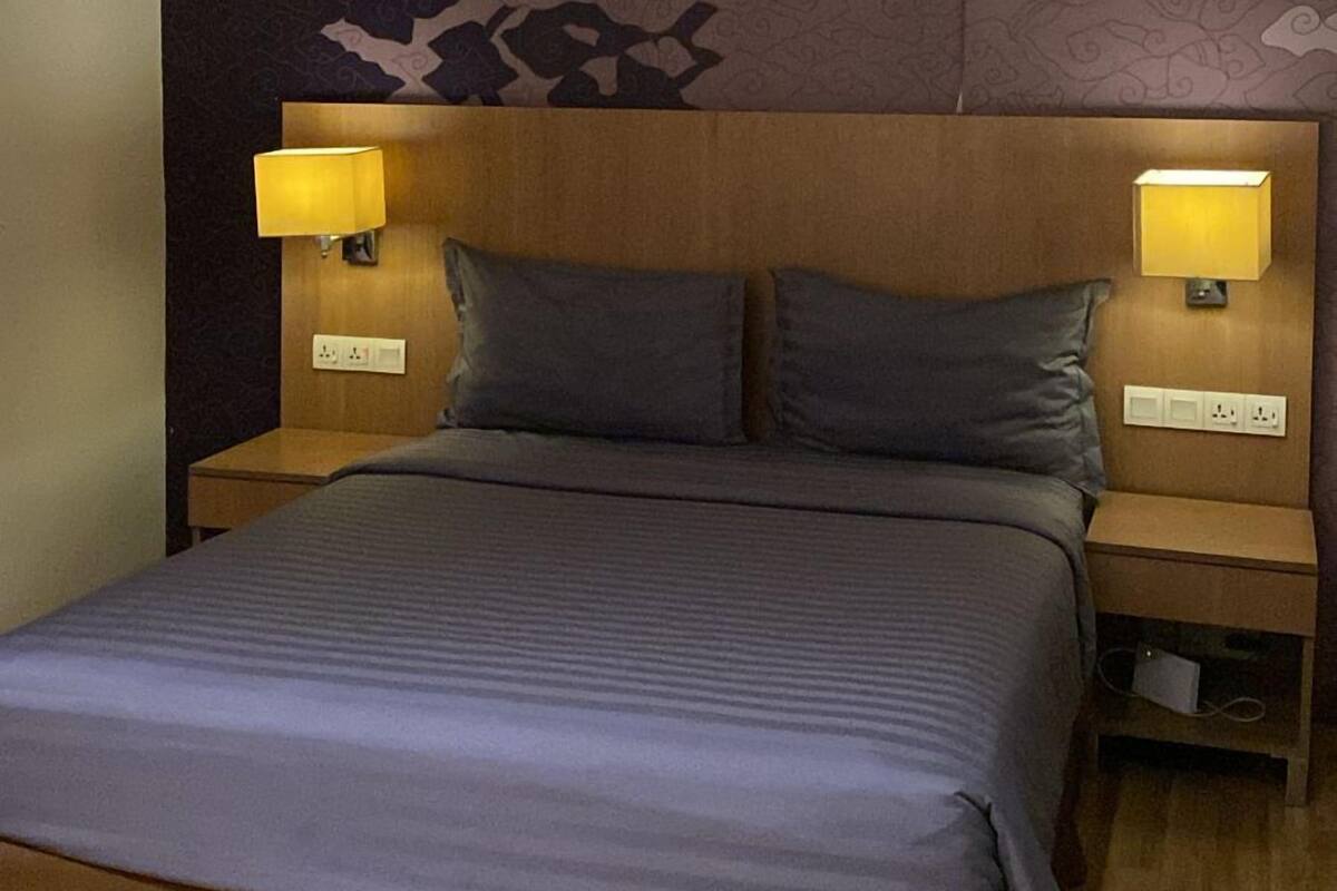 A hotel room with a large bed, two bedside lamps, a headboard with a patterned design, and a wooden floor.