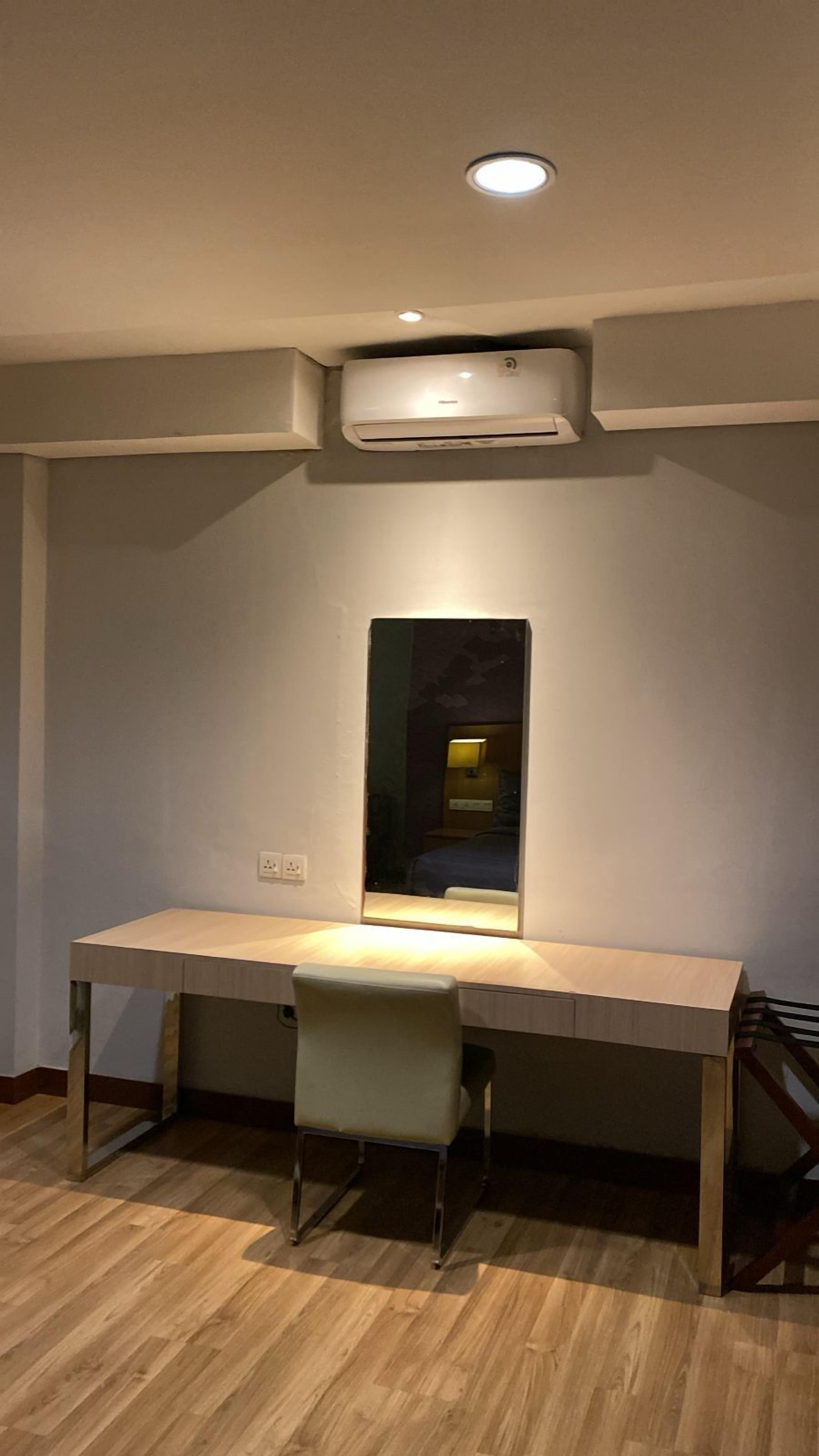 A room with a desk, a chair, an air conditioning unit, and a mirror.