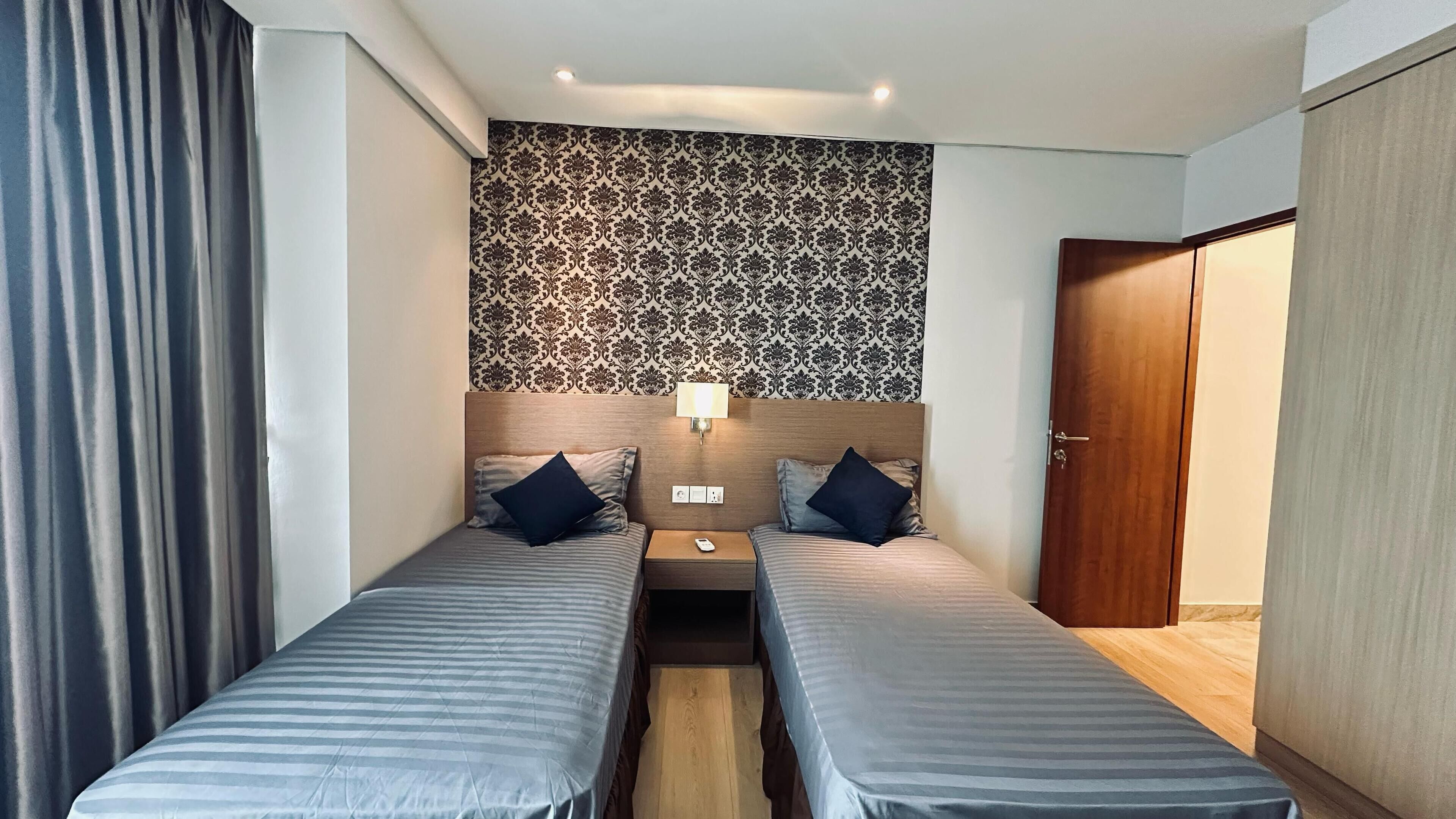 Een hotelkamer met twee enkele bedden, een houten hoofdbord, behang met een patroon, een bedlampje en een deur.