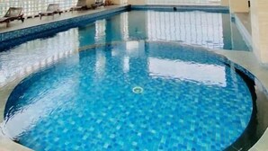 Une piscine intérieure à l’eau d’un bleu limpide, entourée de murs carrelés et surmontée d’un plafond doté d’un luminaire.