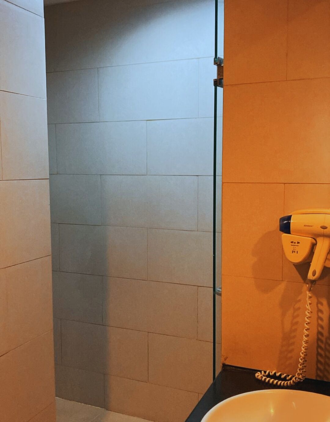 A bathroom with a glass shower door, a yellow hairdryer, and a sink.