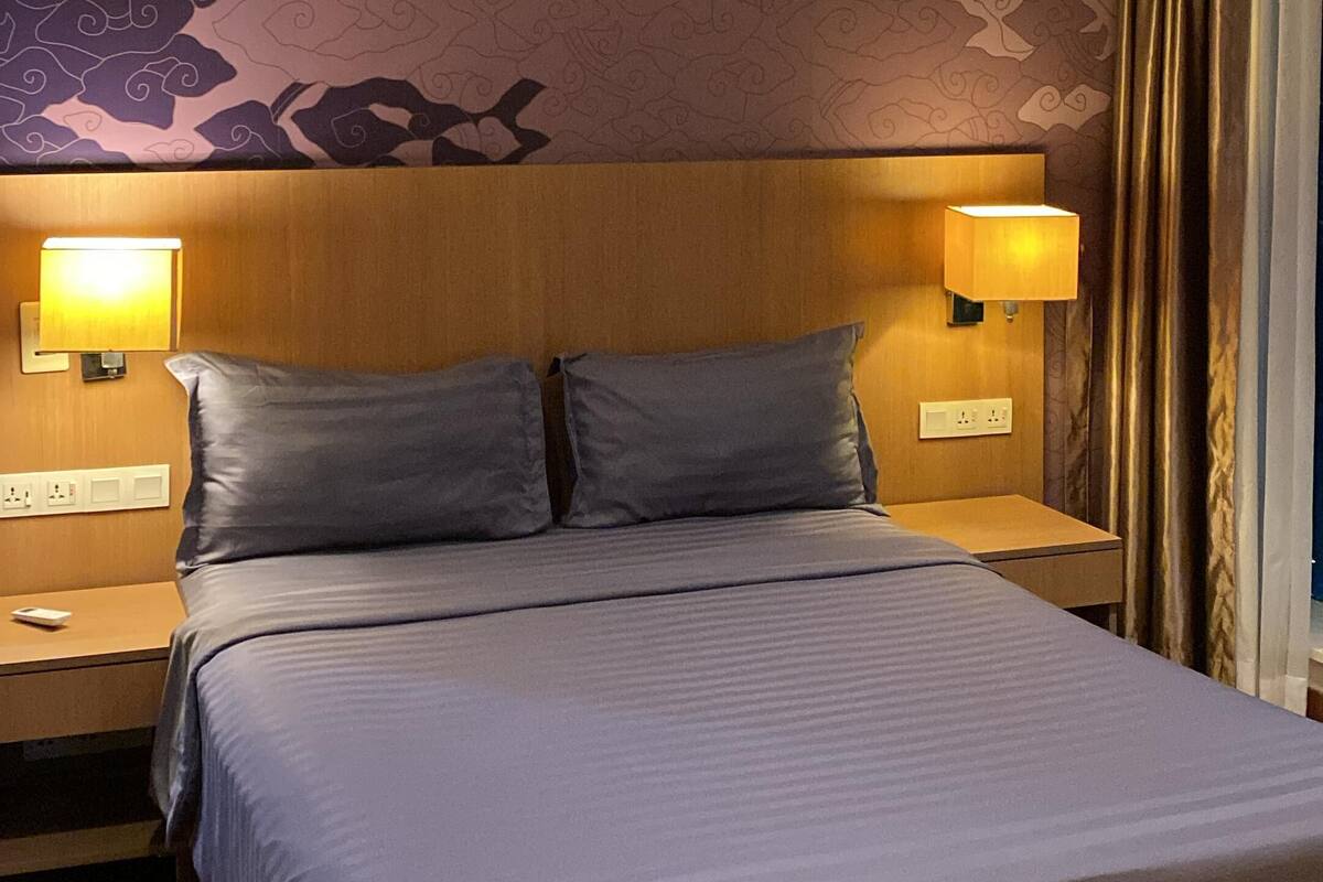 A hotel room with a large bed, two bedside lamps, a wooden headboard, and a patterned wall.