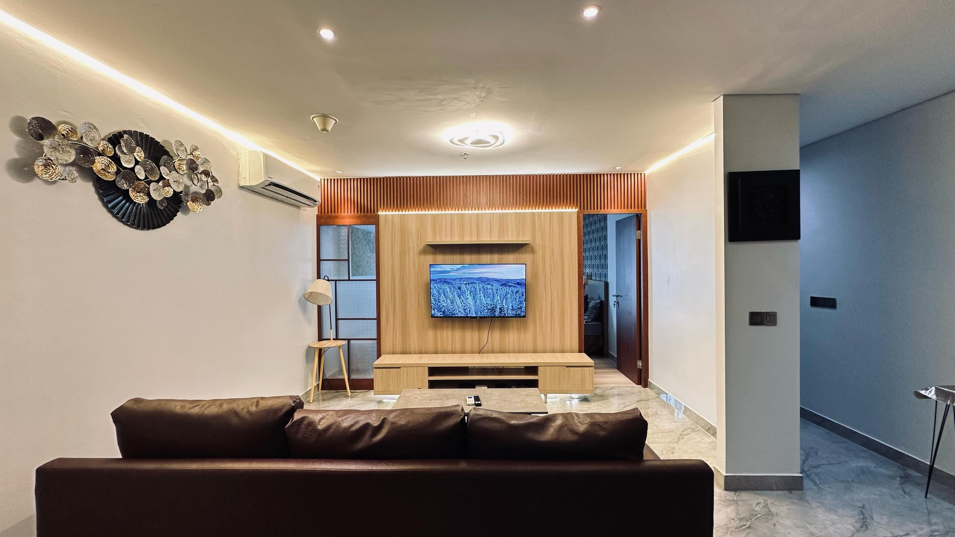 A modern living room with a flat-screen TV mounted on a wooden wall, a leather sofa, and a small side table.