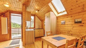 Una cabaña acogedora con interior de madera, un comedor con mesa y sillas, una cocina con refrigerador y pileta, y un ventanal que proporciona luz natural.