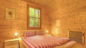 Un dormitorio rústico de cabaña con cama, lámparas de noche, ventana y calefactor.