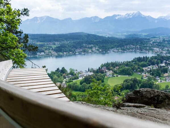 A wooden viewing platform overlooking a lake with a town and mountains in the distance.