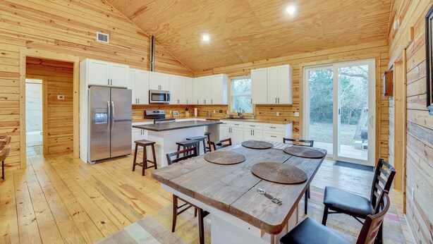 Una cocina moderna con paredes de madera, una isla central y un comedor con una mesa grande y sillas.