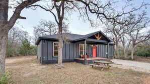 Una cabaña moderna con un porche, una puerta roja y una mesa de picnic.