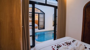 A bedroom with a large bed, a view of a swimming pool, and a glass door leading to a bathroom.