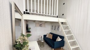 A loft-style room with a white staircase, a blue sofa, and a white desk with a vase of flowers.
