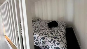 A small, single-bed room with a floral-patterned bedspread, a black pillow, and a white headboard.
