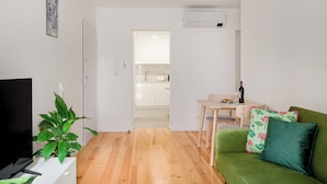 Una sala de estar con un sofá verde, una mesa de comedor con sillas, un televisor y una planta en maceta.