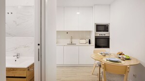 Una cocina moderna con armarios blancos, horno empotrado y comedor con mesa y sillas de madera.