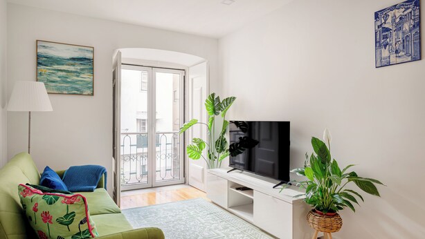 Una sala de estar con un sofá verde, un televisor de pantalla plana, una planta en maceta y un balcón.