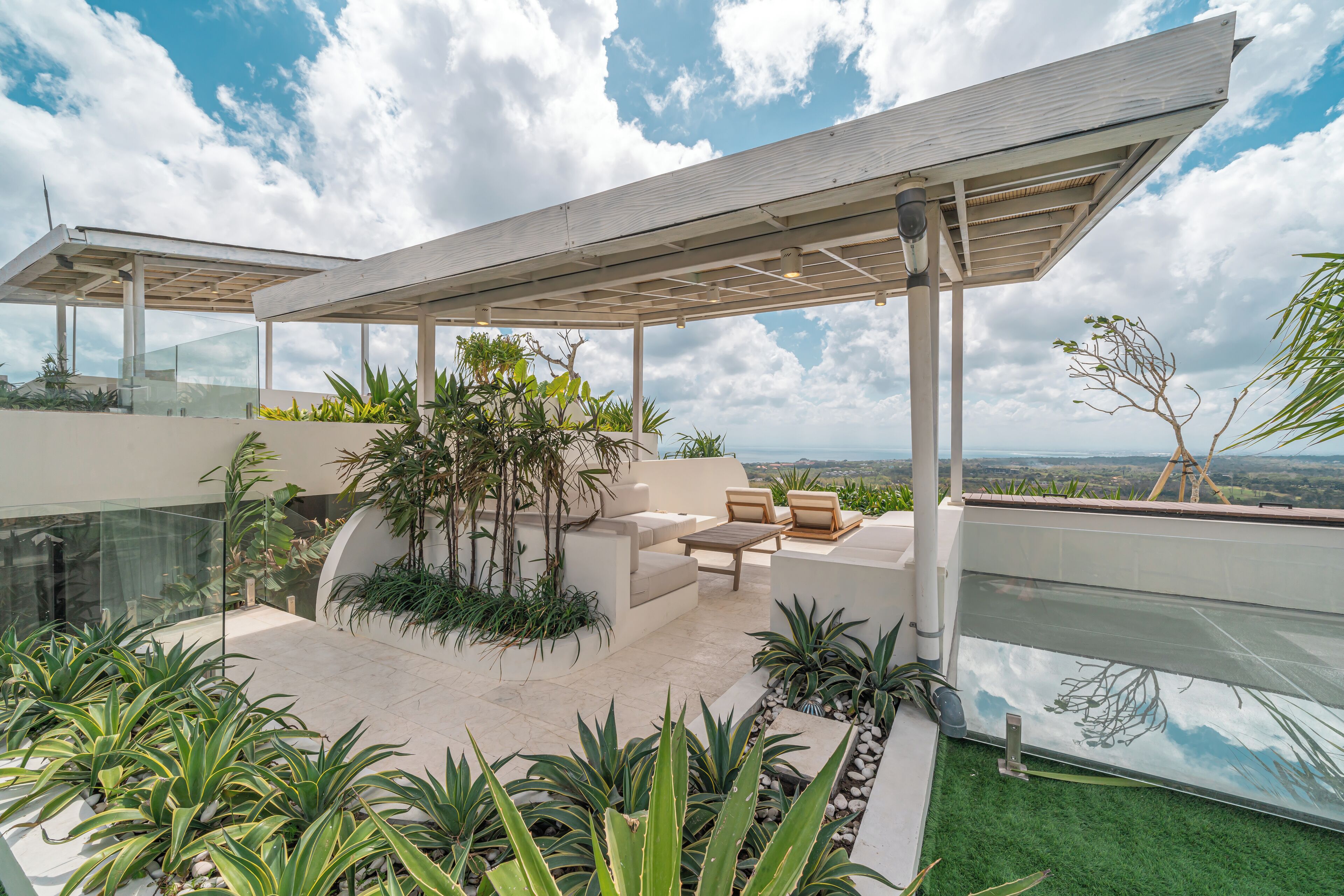 A modern outdoor patio with a glass balustrade, cushioned seating, and a view of the landscape.