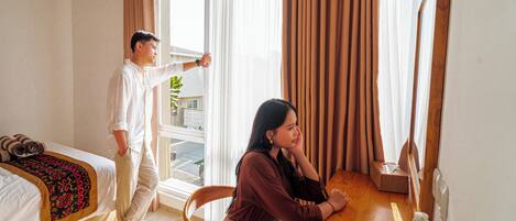 A hotel room with a bed, a wooden desk, and a window with curtains.