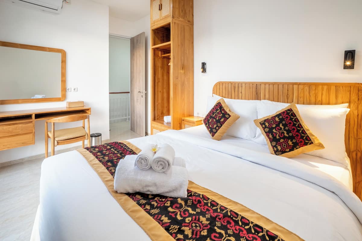 A hotel room with a large bed, a wooden wardrobe, a desk, and a mirror.