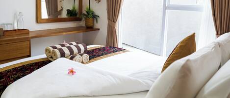 A hotel room with a bed, a wooden dresser, a mirror, a window with curtains, and a potted plant.