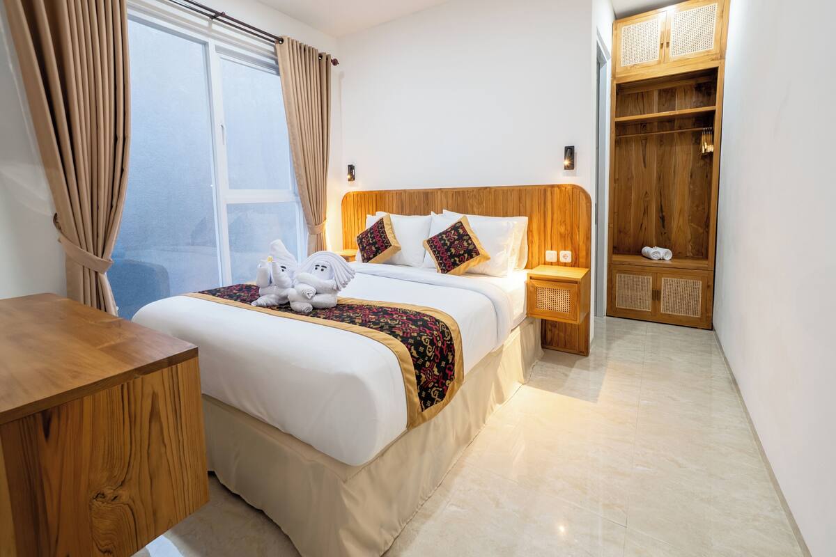 A hotel room with a wooden bed, a desk, a wardrobe, and a window with curtains.