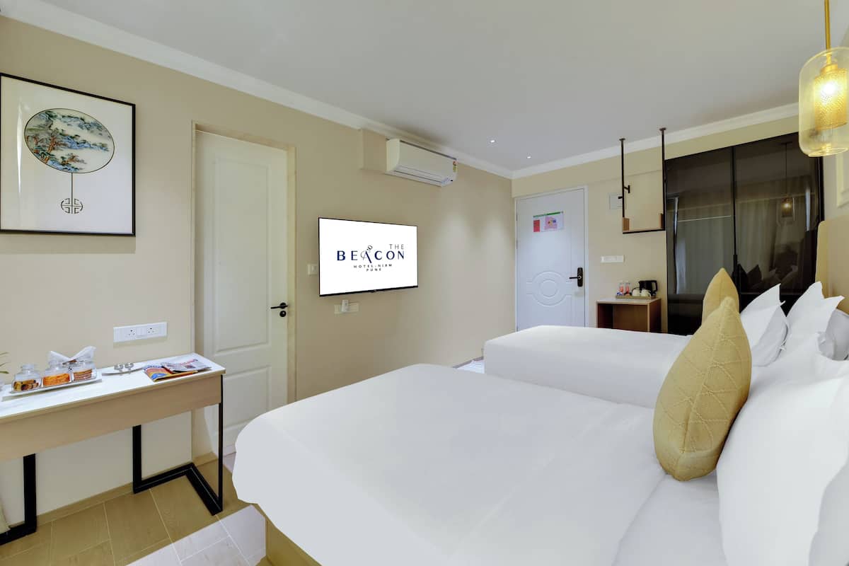 Une chambre d’hôtel avec deux lits, un bureau avec un ordinateur, une télévision et un tableau encadré au mur.