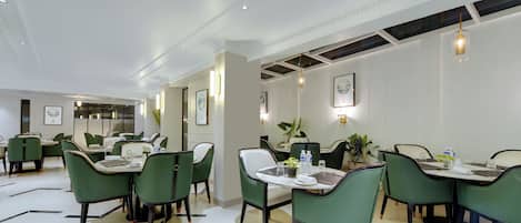 A modern dining area with green chairs, white tables, and black-tiled floors.