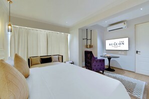 A hotel room with a large bed, a small table, a purple armchair, and a mounted TV displaying "The Beacon Hotel, Mumbai". - The Beacon Hotel NIBM Pune (Pune)