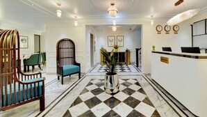 A hotel lobby with a check-in counter, a reception desk, a seating area with a blue chair, and a decorative plant in the center. - The Beacon Hotel NIBM Pune (Pune)