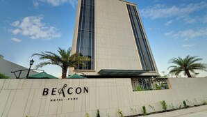 A modern hotel building with a prominent vertical design, palm trees, and a clear sky. - The Beacon Hotel NIBM Pune (Pune)