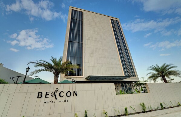 A modern hotel building with a prominent vertical design, palm trees, and a clear sky. - The Beacon Hotel NIBM Pune (Pune)