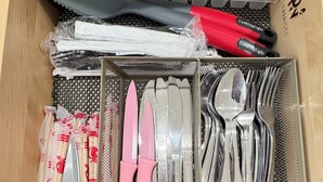 Un cajón con utensilios de cocina ordenados, incluyendo un par de tijeras, cuchillos con mango rosa y una espátula con mango rojo.