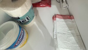 Zona de almacenamiento con un envase grande de lejía Clorox, un paquete rojo y una bolsa de plástico blanca etiquetada para niños.