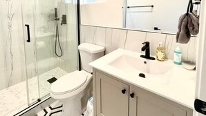 Un baño moderno con ducha de vidrio, inodoro, lavamanos con espejo y suelo estampado.