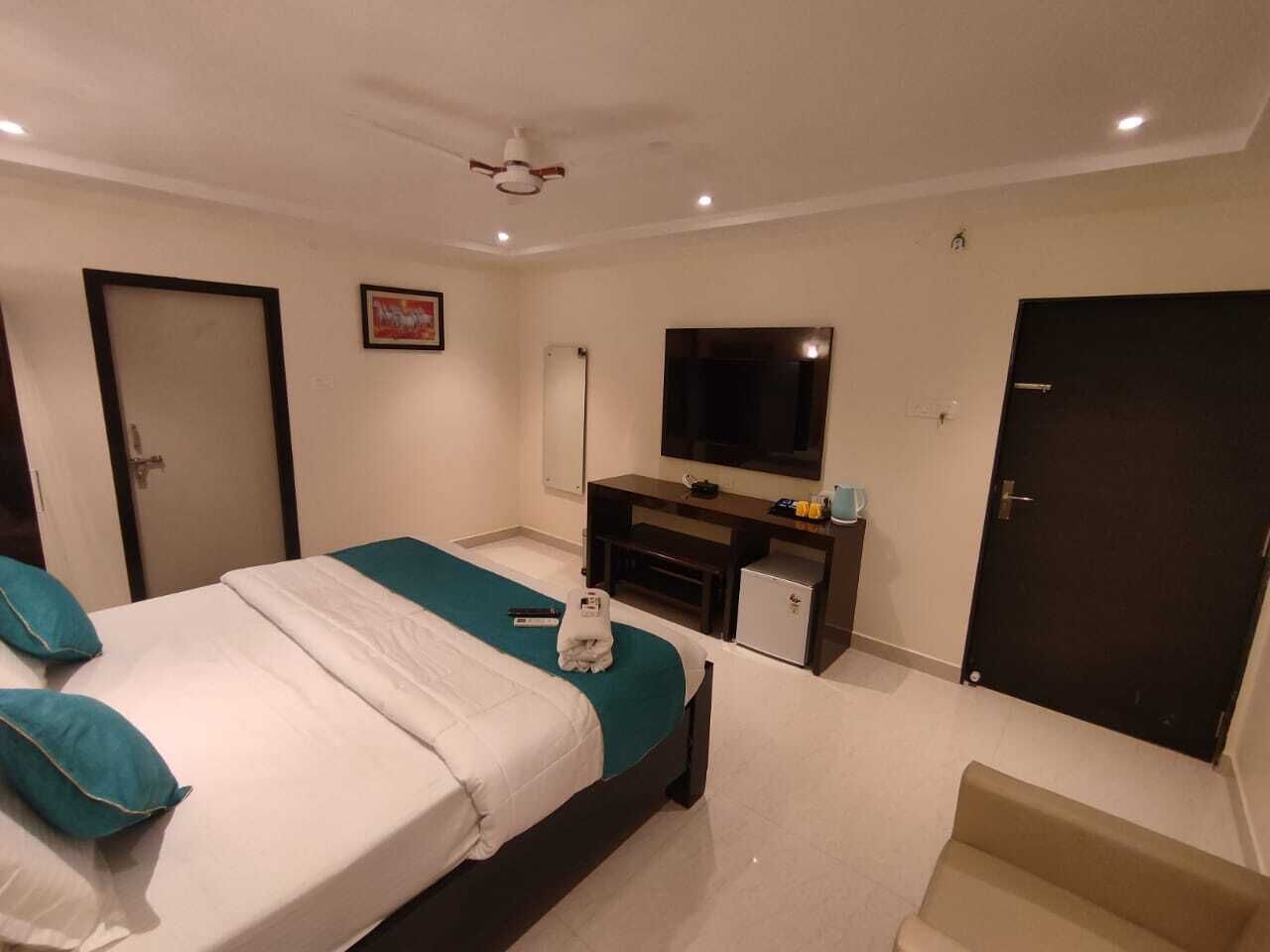 A hotel room with a bed, a desk with a TV, a door, and a small cabinet.