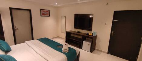 A hotel room with a bed, a desk with a TV, a door, and a small cabinet.