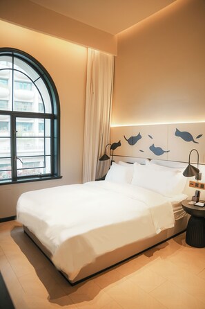 A modern hotel room with a large bed, a bedside table with a lamp, a window with curtains, and a wall with fish-themed artwork. - Lingshe1927 Hotel (Wuhan)