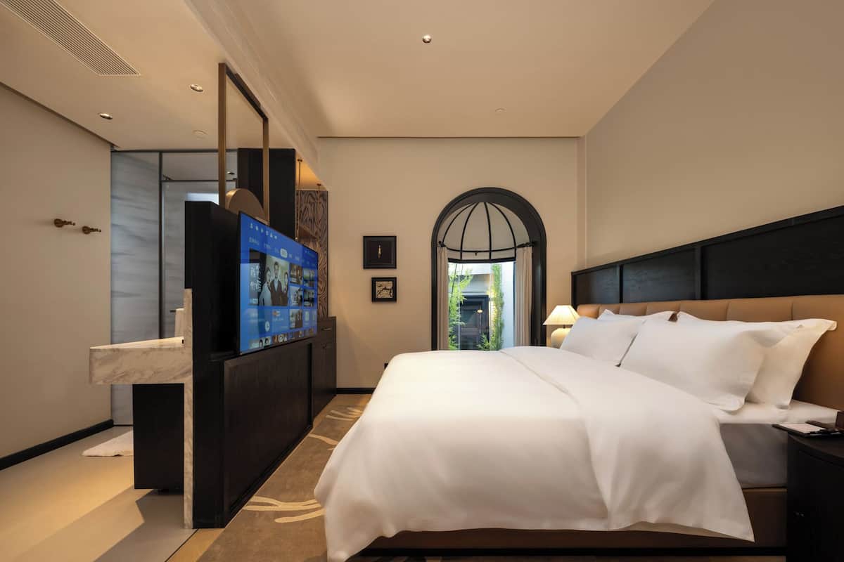 A modern hotel room with a large bed, a vanity with a mirror, and a television mounted on the wall.