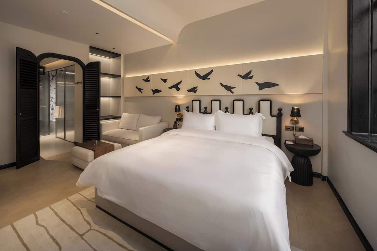 A modern bedroom with a large bed, a seating area, and a walk-in closet.
