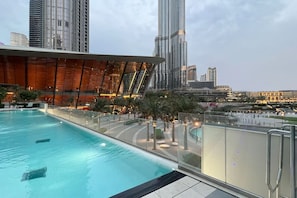 A swimming pool with a glass barrier, surrounded by palm trees and modern buildings in the background. - Gogoto1 2BR Burj Khalifa, Fountain View Dubai Mall (Dubai)