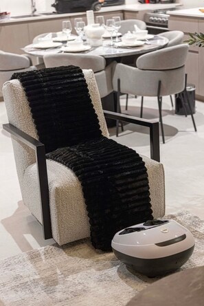 A modern living room with a light-colored armchair, a black throw blanket, and a robotic vacuum cleaner. - Gogoto1 2BR Burj Khalifa, Fountain View Dubai Mall (Dubai)