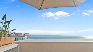 A balcony with a view of the sea, a potted plant, and a modern building in the background. - Marsala 201: 2BR w/ Rooftop Pool - Walk to Beach (Bucerías)